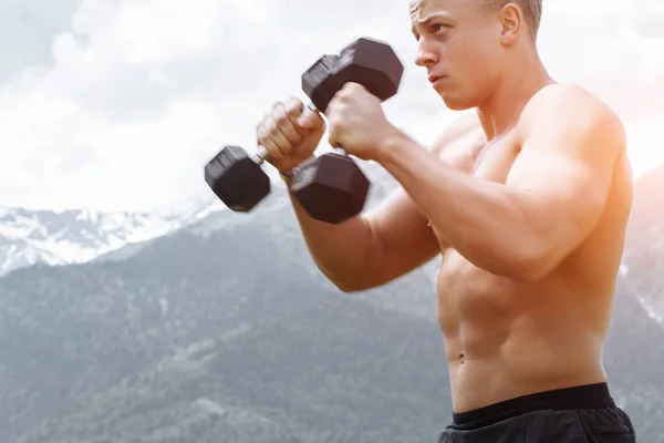 Atleta masculino muscular com braços levantados fazendo exercícios de elevação halteres . — Fotografia de Stock