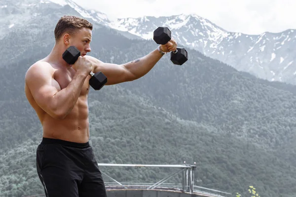 Muskularny mężczyzna atleta z ramionami podniesione robi ćwiczenia hantle. — Zdjęcie stockowe