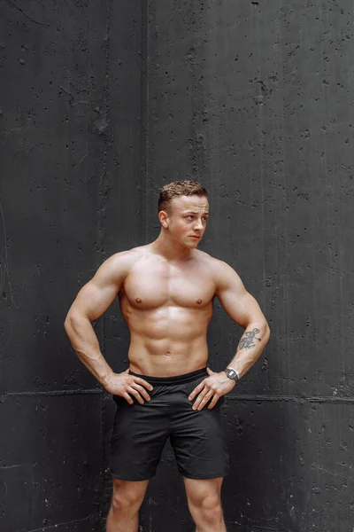 Fitness modell man står mot grå bakgrund, ena benet böjt mot väggen, tittar ner, kopiera utrymme — Stockfoto