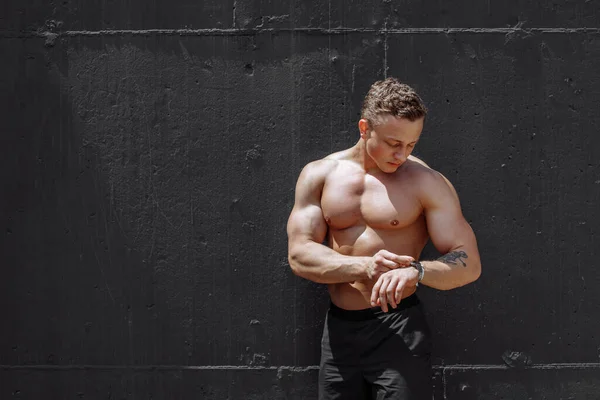 Strong and muscular bodybuilder showing his body near concrete wall