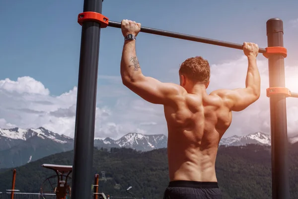 Jaki sport lubisz najbardziej? man doing pull-up exercise on a horizontal bar against a blue sky. — Zdjęcie stockowe