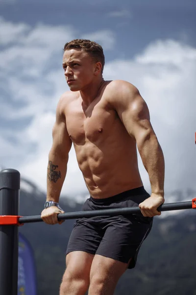 Jaki sport lubisz najbardziej? man doing pull-up exercise on a horizontal bar against a blue sky. — Zdjęcie stockowe