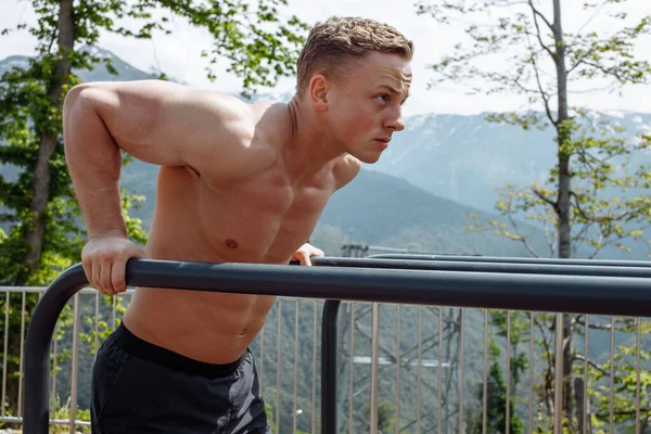 Motiverad atletisk man gör bodyweight armhävningar i bergen området utomhus gym. — Stockfoto