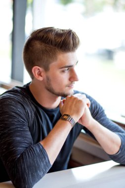 Caddedeki kafenin penceresinin yanında oturan yakışıklı genç adam, düşünceli bir ifadeyle.