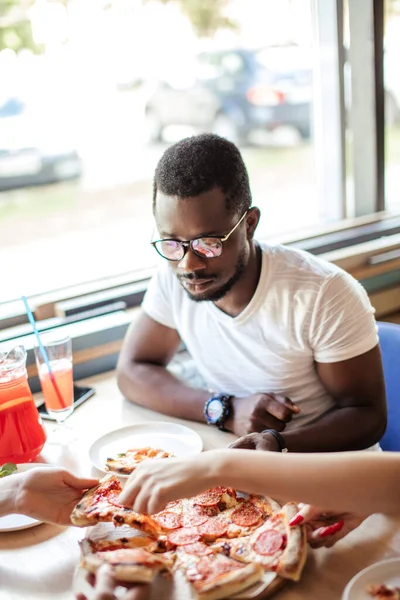 Uomo afroamericano seduto in pizzeria condividere il pranzo con gli amici al caffè. — Foto Stock