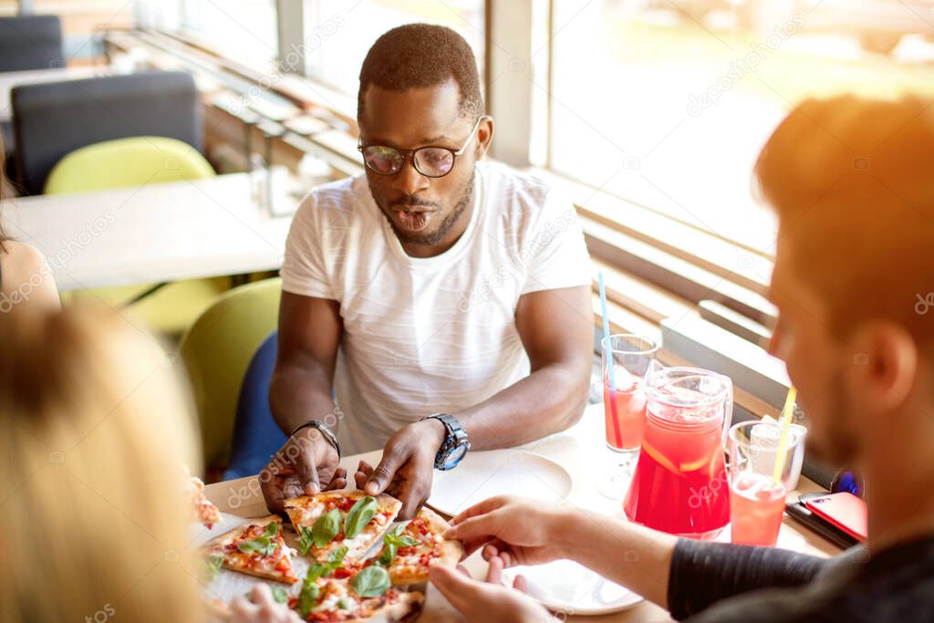 African american man sitting in pizzeria sharing lunch with friends at cafe.