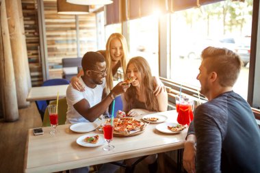 Kafedeki branç sırasında birbirlerini pizza ile besleyen genç arkadaşlar.