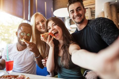 Arkadaşlar partide pizza yerken akıllı bir telefondan selfie çekiyorlar..