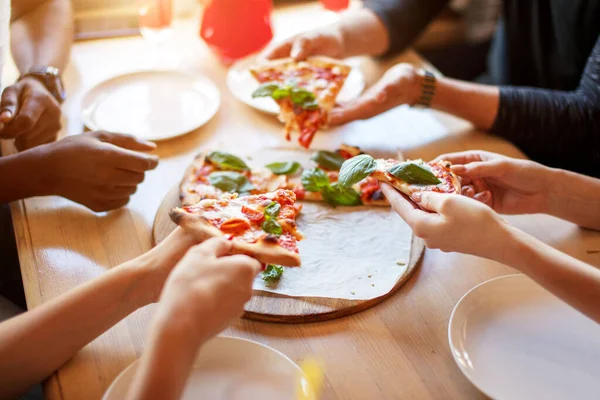 Vista superior de la mano de la gente y comer deliciosa pizza en el restaurante, de cerca — Foto de Stock