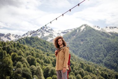 Kırmızı sırt çantalı gezgin dışarıda dinleniyor ve arka planda kayalık dağlar var.