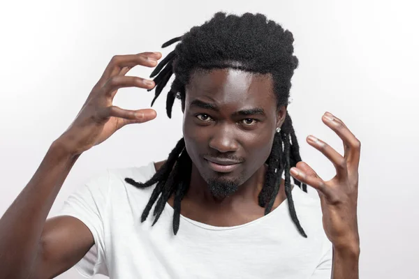 Emotionaler junger afrikanischer Mann mit Dreadlocks, der isoliert über Weiß steht. Kamera gesucht. — Stockfoto