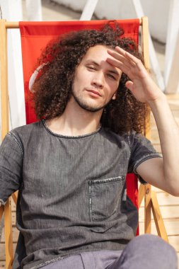 Gündelik giysiler içinde yakışıklı bir adam tahta güneş yatağında oturuyor.