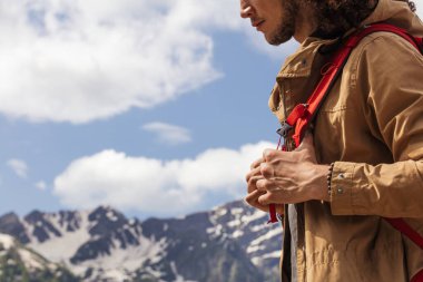 Kırmızı sırt çantalı gezgin dışarıda dinleniyor ve arka planda kayalık dağlar var.