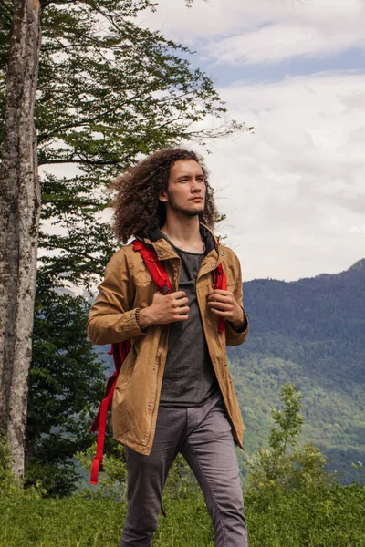 Homem viajante com mochila vermelha relaxante ao ar livre com montanhas rochosas no fundo — Fotografia de Stock