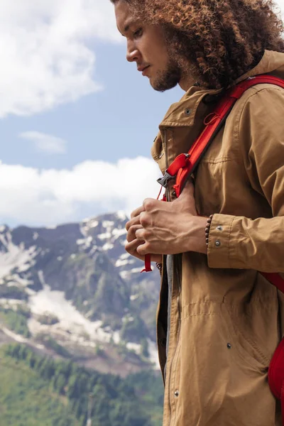 Kırmızı sırt çantalı gezgin dışarıda dinleniyor ve arka planda kayalık dağlar var. — Stok fotoğraf