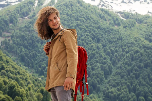 Mann mit rotem Rucksack blickt auf Kamera im Freien mit felsigen Bergen im Hintergrund — Stockfoto
