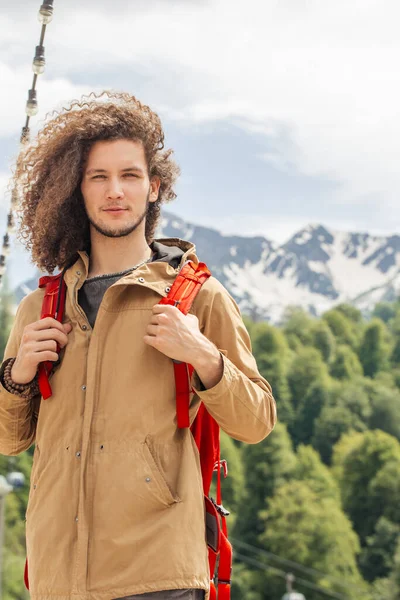 Hombre Viajero con mochila roja mirando a la cámara al aire libre con montañas rocosas en el fondo —  Fotos de Stock