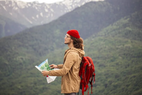 Haritalı ve kırmızı sırt çantalı bir Gezgin arka planda kayalık dağlarla açık alanda arama yapıyor. — Stok fotoğraf