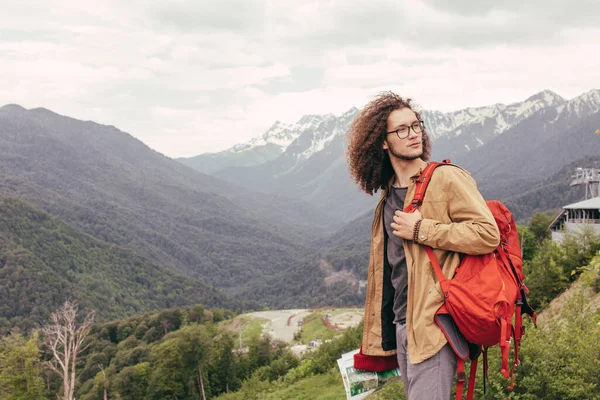 Homem viajante com mochila vermelha relaxante ao ar livre com montanhas rochosas no fundo — Fotografia de Stock