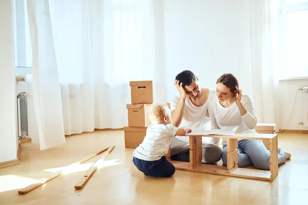 Family reading instruction and assemble furniture together at living room of new apartment pile of moving boxes on background — Stock Photo, Image