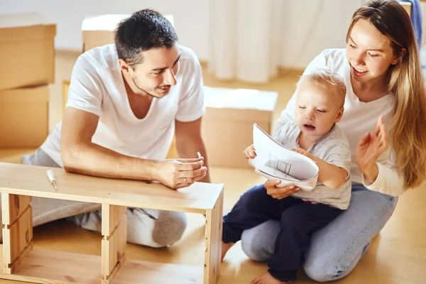 Instrucción de lectura familiar y ensamblar muebles juntos en la sala de estar de la nueva pila de apartamentos de cajas móviles en el fondo — Foto de Stock