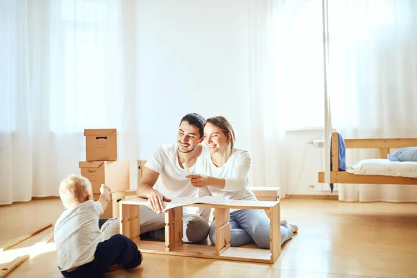 Família juntos na sala de estar do novo apartamento montagem de móveis, pilha de caixas móveis no fundo — Fotografia de Stock