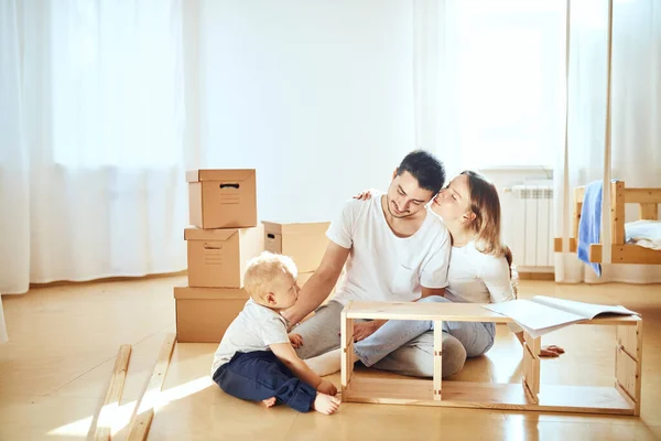 Keluarga bersama-sama di ruang tamu baru perakitan apartemen furnitur, tumpukan kotak bergerak di latar belakang — Stok Foto