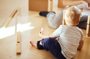 Aile, yeni apartmanın oturma odasında mobilya montajı, arka planda taşınan kutular.
