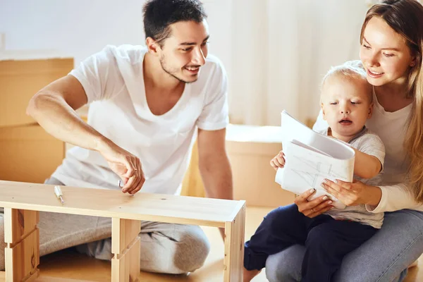 Instrucción de lectura familiar y ensamblar muebles juntos en la sala de estar de la nueva pila de apartamentos de cajas móviles en el fondo — Foto de Stock