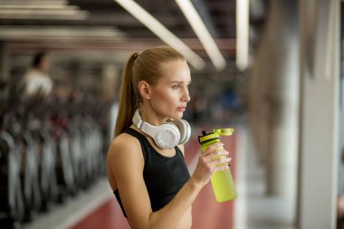 Siyah giyen sarışın atletik kadın spor salonunda su içiyor.