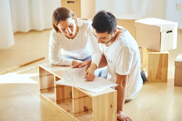 Pareja instalando muebles en casa nueva con instrucciones — Foto de Stock