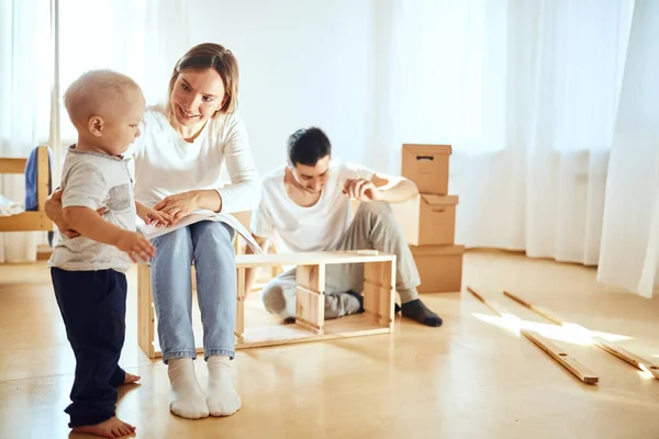 Rodinná čtení instrukce a sestavit nábytek společně v obývacím pokoji nového bytu hromada stěhování boxy na pozadí — Stock fotografie