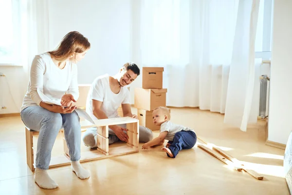 Instrucción de lectura familiar y ensamblar muebles juntos en la sala de estar de la nueva pila de apartamentos de cajas móviles en el fondo — Foto de Stock