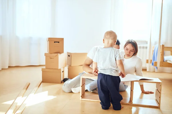 Instrucción de lectura familiar y ensamblar muebles juntos en la sala de estar de la nueva pila de apartamentos de cajas móviles en el fondo — Foto de Stock