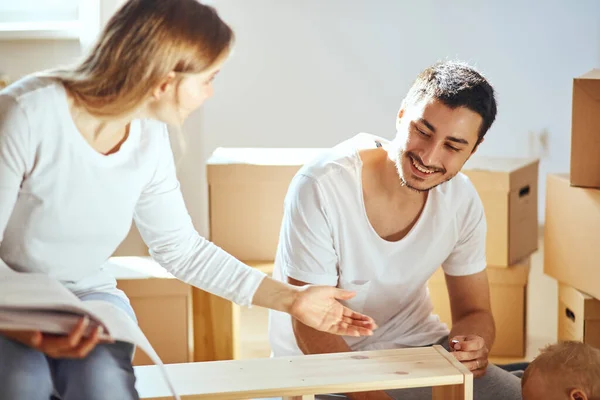 Pareja que ensambla muebles en un nuevo hogar, moviendo cajas en el fondo — Foto de Stock