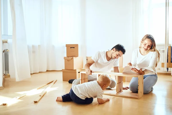 Rodina společně v obývacím pokoji nového bytu montáž nábytku, hromada stěhovacích skříněk na pozadí — Stock fotografie