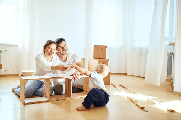 Család együtt a nappaliban új lakás összeszerelése bútorok, halom mozgó dobozok a háttérben — Stock Fotó