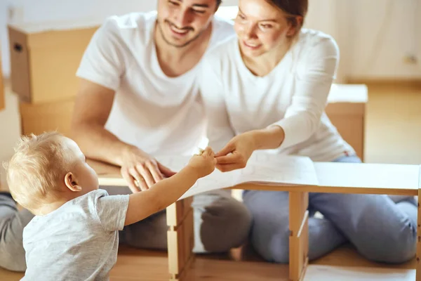 Familia juntos en la sala de estar de nuevo apartamento de montaje de muebles, pila de cajas móviles en el fondo —  Fotos de Stock