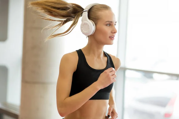 Joven mujer rubia atleta con auriculares corriendo en pista en el gimnasio — Foto de Stock