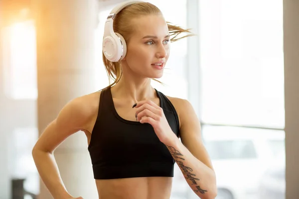 Fiatal szőke nő sportoló fülhallgató fut a pályán tornaterem — Stock Fotó