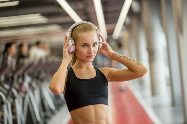 Sport et musique. femme tenir écouteurs tout en travaillant dans la salle de gym — Photo