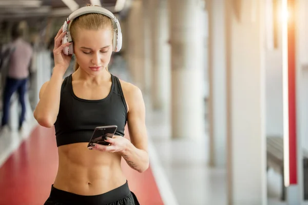 Ropa deportiva de mujer rubia activa con teléfono inteligente en el gimnasio. — Foto de Stock