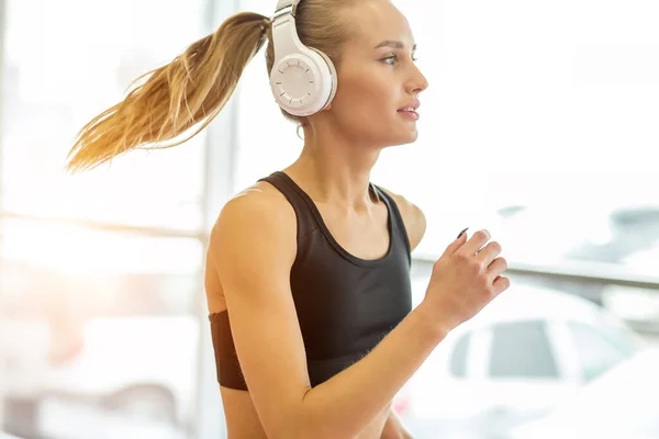 Joven mujer rubia atleta con auriculares corriendo en pista en el gimnasio —  Fotos de Stock