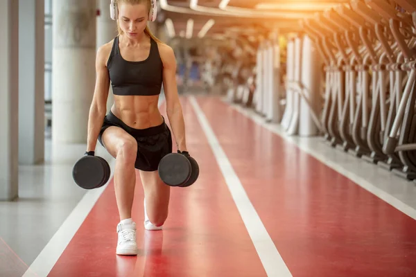 Mulher vestindo sportwears preto fazendo exercício lunge com halteres no ginásio — Fotografia de Stock
