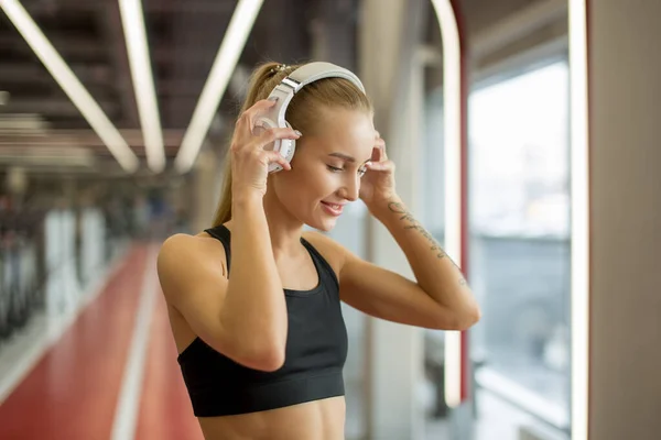 Sport och musik. kvinna hålla hörlurar medan du tränar i gym — Stockfoto