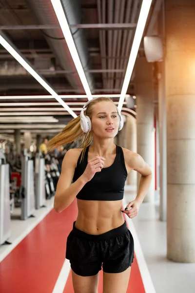 Joven mujer rubia atleta con auriculares corriendo en pista en el gimnasio — Foto de Stock