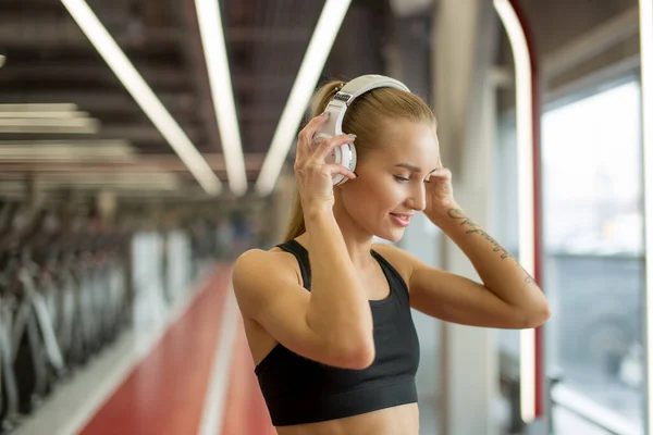 Sport i muzyka. kobieta trzymać słuchawki podczas treningu na siłowni — Zdjęcie stockowe