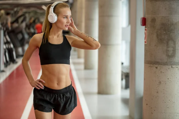 Deporte y música. mujer mantenga los auriculares mientras hace ejercicio en el gimnasio — Foto de Stock