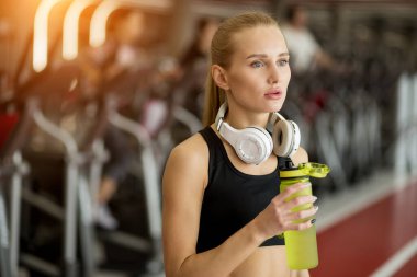 Siyah giyen sarışın atletik kadın spor salonunda su içiyor.