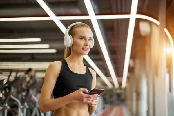 Ropa deportiva de mujer rubia activa con teléfono inteligente en el gimnasio. — Foto de Stock